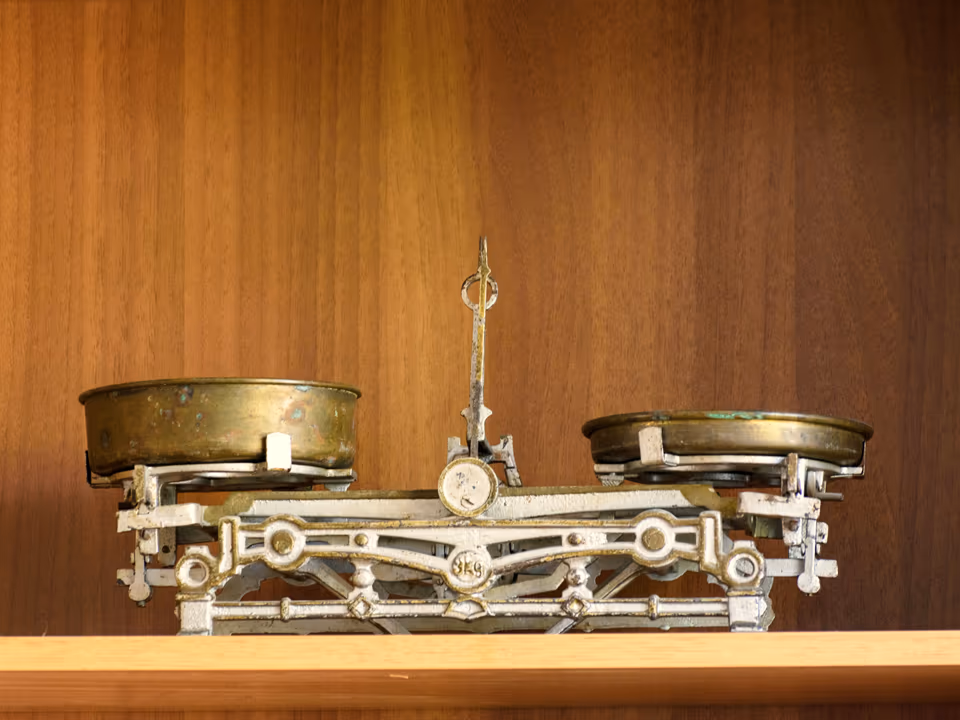 An antique brass balance scale on a warm wooden shelf